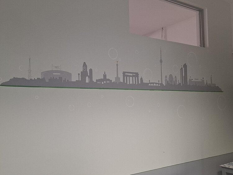 Auf einer Wand unter einem Fenster ist in hellgrauer Farbe die Skyline von Berlin aufgemalt.