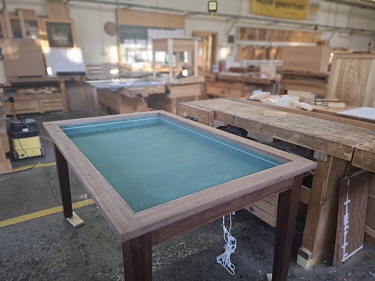 In einer Schreinerwerkstatt steht ein Billardtisch mit Holzrahmen und einer Fläche aus grünem Filz.