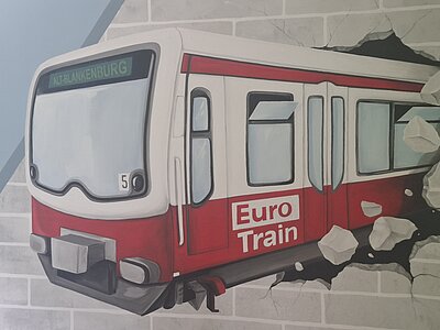 Wandgemälde eines Zuges, der durch eine Steinmauer bricht. Seitlich auf dem Zug steht in rot "Euro-Train", vorne steht "Alt-Blankenburg".